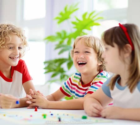 Drei Kinder sitzen lachend am Tisch zuhause und spielen ein Brettspiel