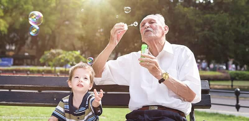 Opa und Enkel sitzen auf der Bank und spielen mit Seifenblasen
