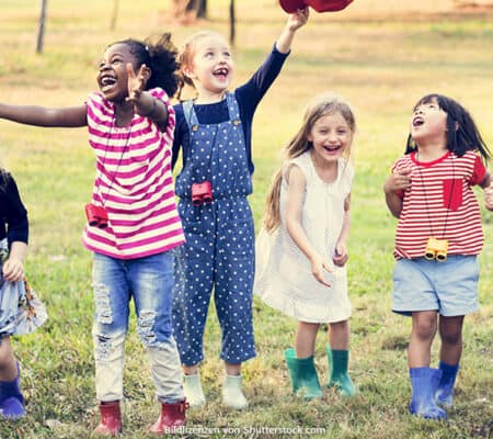 Kinder verschiedener Hautfarben spielen draußen im Regen und lachen.