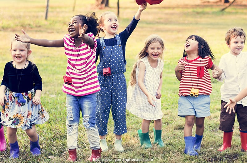 Kinder verschiedener Hautfarben spielen draußen im Regen und lachen.