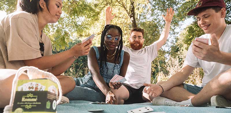 Freunde spielen in der Natur beim Picknick auf einer Decke das grüne Rommé. Internationaler Tag der Erde 2023. ASS Altenburger