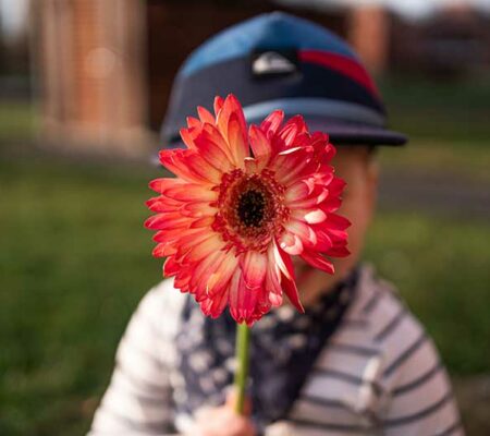 Kind mit roter Blume vor grüner Wiese im Sonnenschein. Farben lernen mit ASS Altenburger.