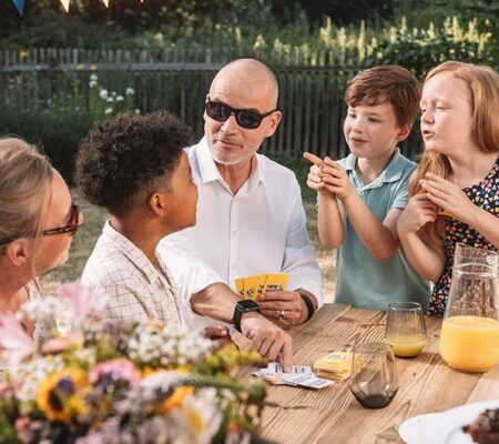 Familie mit Kindern, Opa, Oma und Vater spielt gemeinsam am Tisch im Garten Familienspiele. Familientag, Tag der Familie, ASS Altenburger