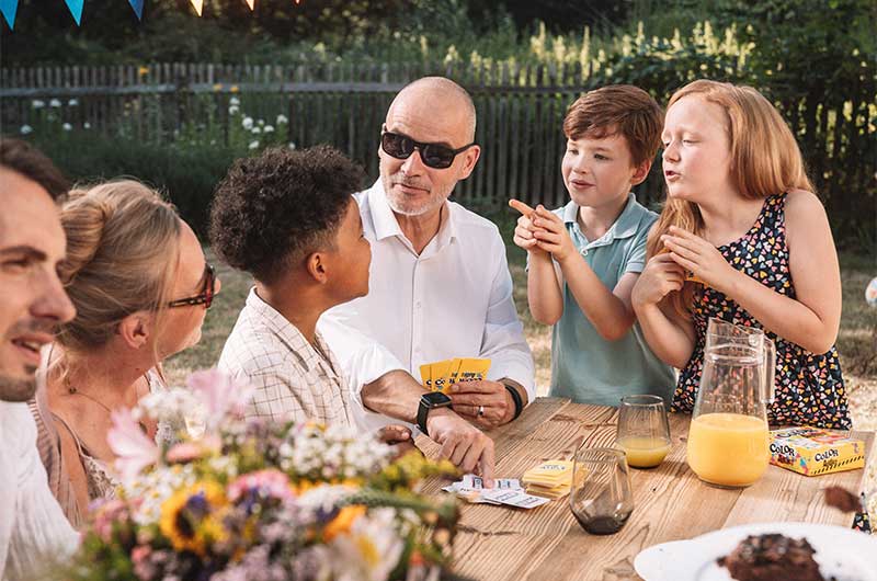 Familie mit Kindern, Opa, Oma und Vater spielt gemeinsam am Tisch im Garten Familienspiele. Familientag, Tag der Familie, ASS Altenburger