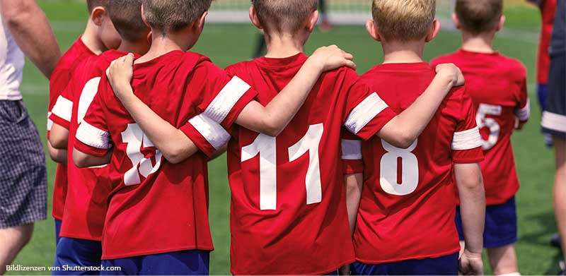Kinder in roten Fußball Trikots mit weißen Nummern sind von hinten zu sehen Arm in Arm. Kinderfußball, ASS Altenburger