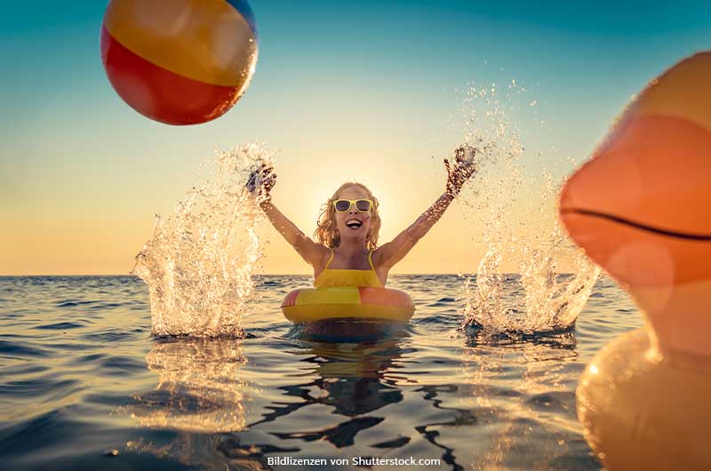 Kind schwimmt im Sommer mit Schwimmreifen im Wasser, trägt Sonnenbrille, lacht und wirft Wasserball. Im Vordergrund schwimmt eine aufblasbare Gummiente. Sommeranfang, ASS Altenburger