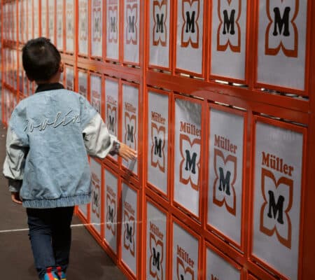 Ein kleiner Junge läuft an einer großen Spielwand mit dem Logo des Spielwarengeschäffts Müller vorbei.