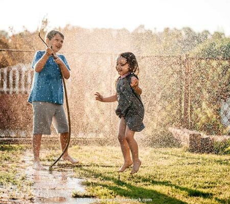 Junge und Mädchen spielen im Garten mit Gartenschlauch und spritzen mit Wasser. Abkühlung bei Hitze, ASS Altenburger