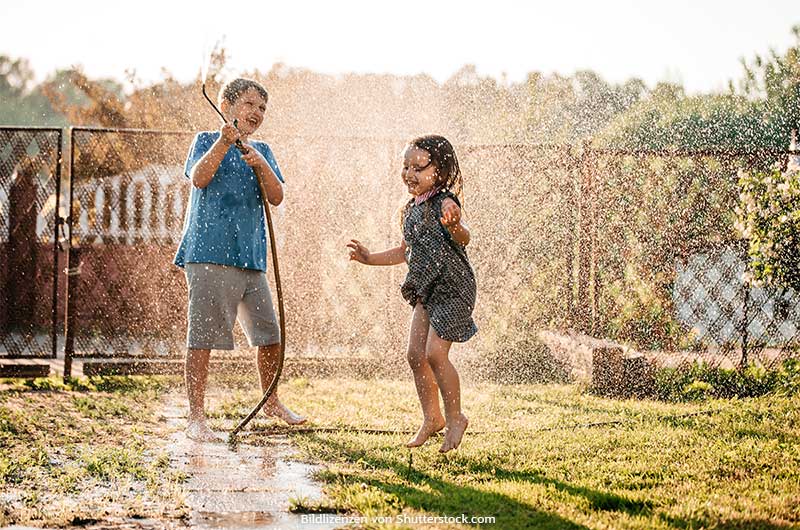 Junge und Mädchen spielen im Garten mit Gartenschlauch und spritzen mit Wasser. Abkühlung bei Hitze, ASS Altenburger