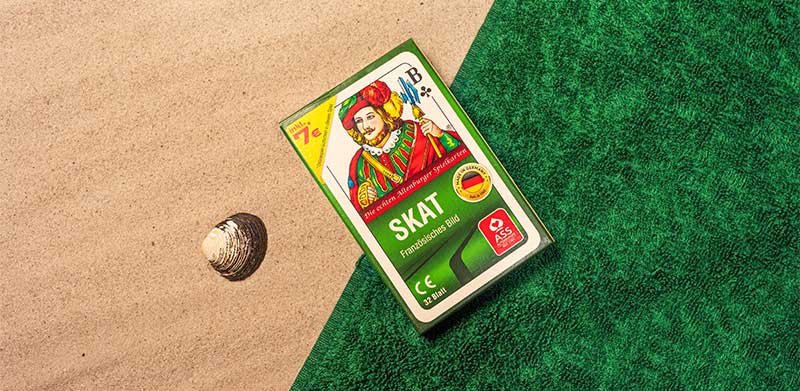 Kartenspiel Skat liegt am Strand neben Muschel auf grünem Handtuch. Abkühlung bei Hitze, ASS Altenburger