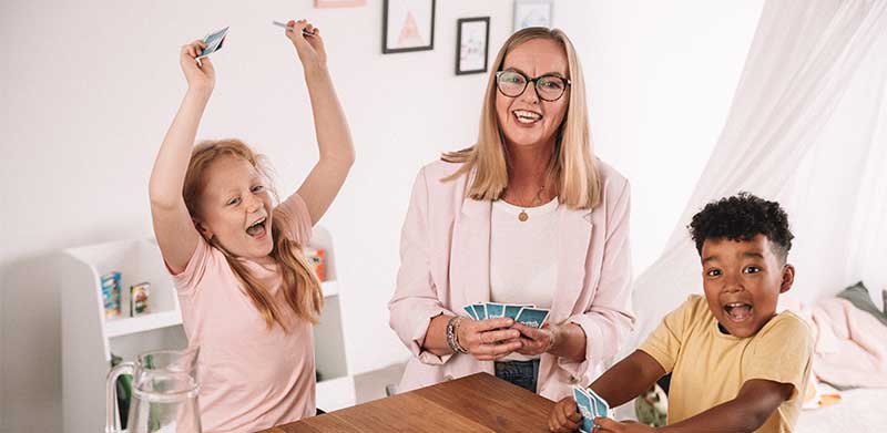 Ein Mädchen und ein Junge spielen im Kinderzimmer Mau Mau mit ihrer Oma, das Mädchen freut sich über ihren Sieg. Beschäftigung für Senioren, ASS Altenburger