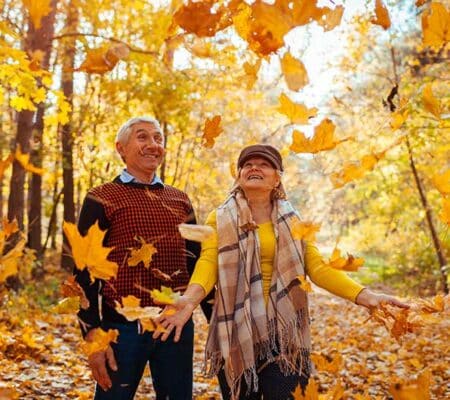 Ein Rentnerpaar geht im Wald spazieren und lacht als die Frau Blätter in die Luft wirft. Beschäftigung für Senioren, ASS Altenburger