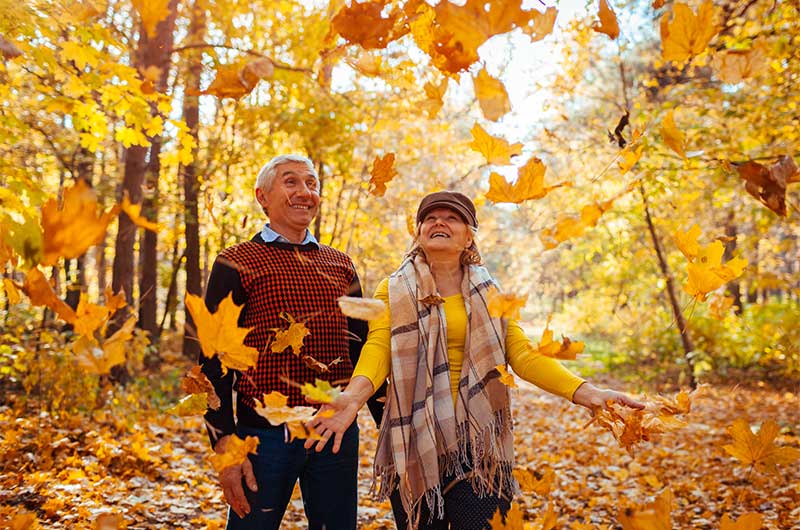 Ein Rentnerpaar geht im Wald spazieren und lacht als die Frau Blätter in die Luft wirft. Beschäftigung für Senioren, ASS Altenburger