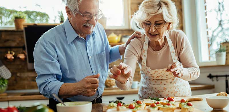 Ein Rentnerpaar hat Spaß daran, in der Küche gemeinsam zu kochen und kleine Schnittchen zu belegen. Beschäftigung für Senioren, ASS Altenburger