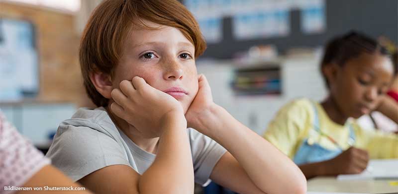 Junge sitzt in der Schule und neben Mädchen, stützt den Kopf auf den Händen ab und schaut verträumt in die Ferne. Aufmerksamkeit, ASS Altenburger