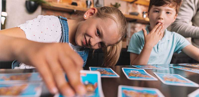 Mädchen und Junge spielen Paw Patron Memo, das Mädchen schaut vorsichtig unter eine Karte und lächelt, der Junge ist überrascht und hält die Hand vor den Mund. Aufmerksamkeit, ASS Altenburger