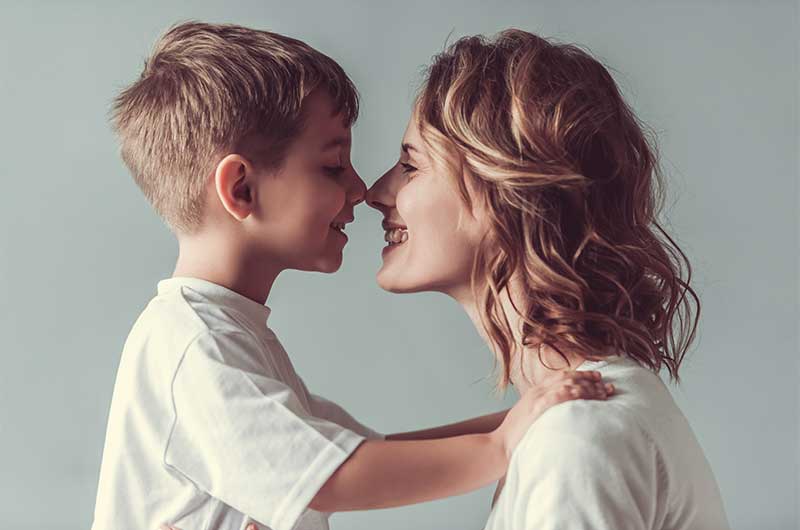 Mutter und Sohn stehen sich gegenüber und lächeln sich an. Ihre Nasen berühren sich, das Kind legt die Hände auf die Schultern der Mutter. Aufmerksamkeit, ASS Altenburger