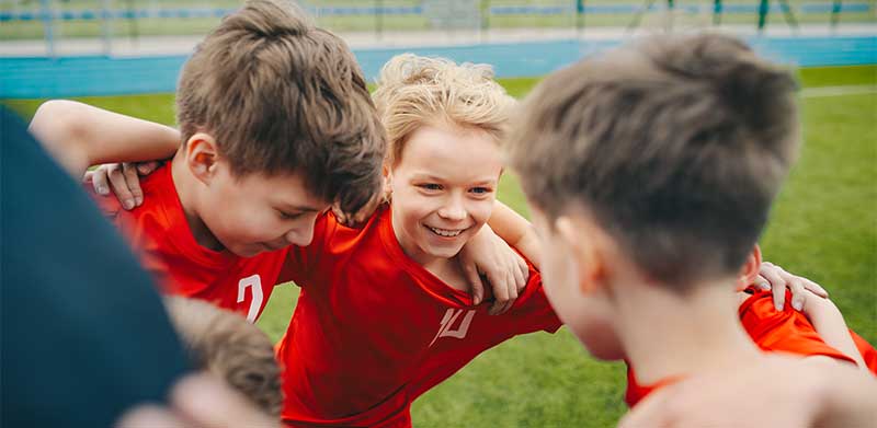 Kinder stehen in rotem Trikot Arm in Arm auf dem Fußballplatz, lachen und bilden einen Kreis. Ehrgeiz, ASS Altenburger