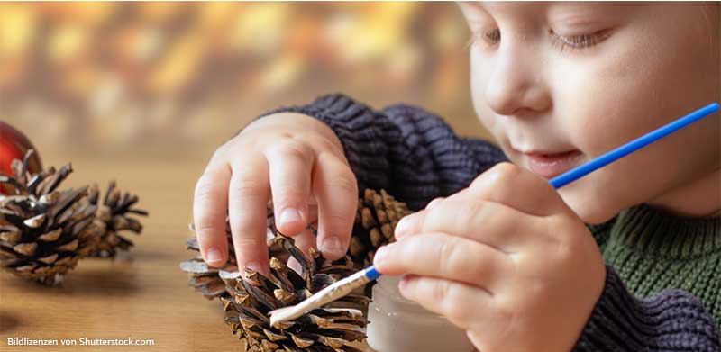 Junge malt Tannenzapfen mit blauem Pinsel an. Basteln mit Kindern zu Weihnachten, ASS Altenburger