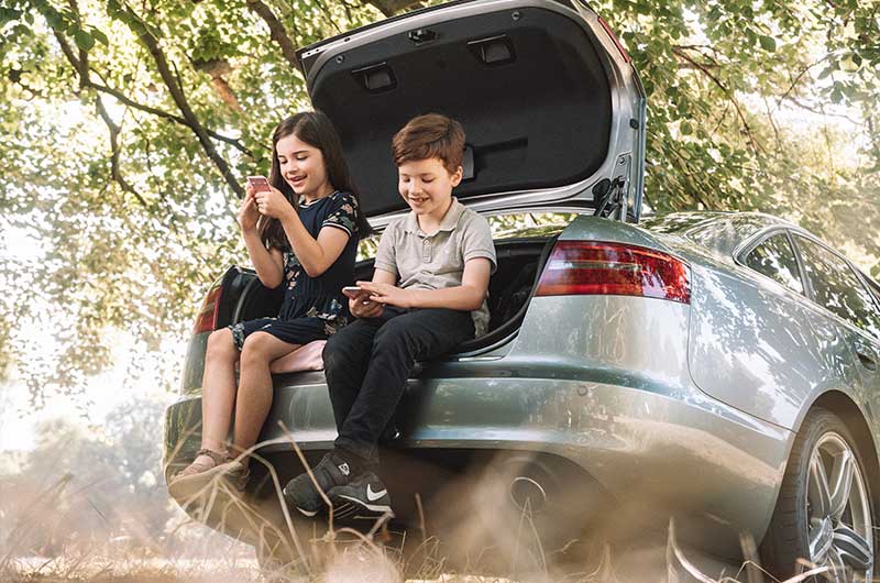 Junge und Mädchen sitzen auf Rand vom Kofferraum eines silbernen Autos und spielen Karten. Kartenspiele zu zweit, ASS Altenburger