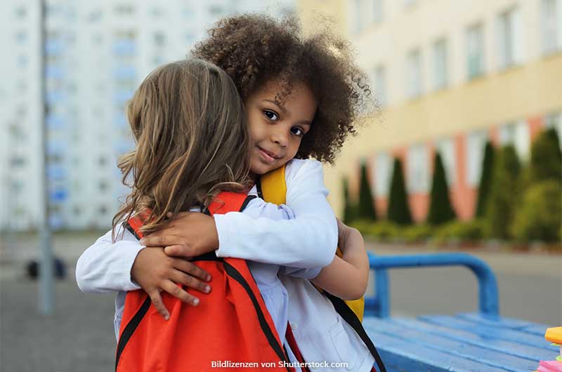 Zwei-Maedchen-umarmen-sich-und-eins-davon-blickt-in-die-Kamera-Soziale-Kompetenz-bei-Kindern-ASS-Altenburger