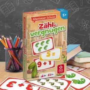 Das Abenteuer Schule Zählvergnügen Spiel steht auf einem Schultisch. Unter dem Tisch liegen einige der dazugehörigen Spielkarten. Neben dem Spiel stehen Stifte und ein Bücherstapel. Im Hintergrund ist unscharf eine Tafel zu erkennen.