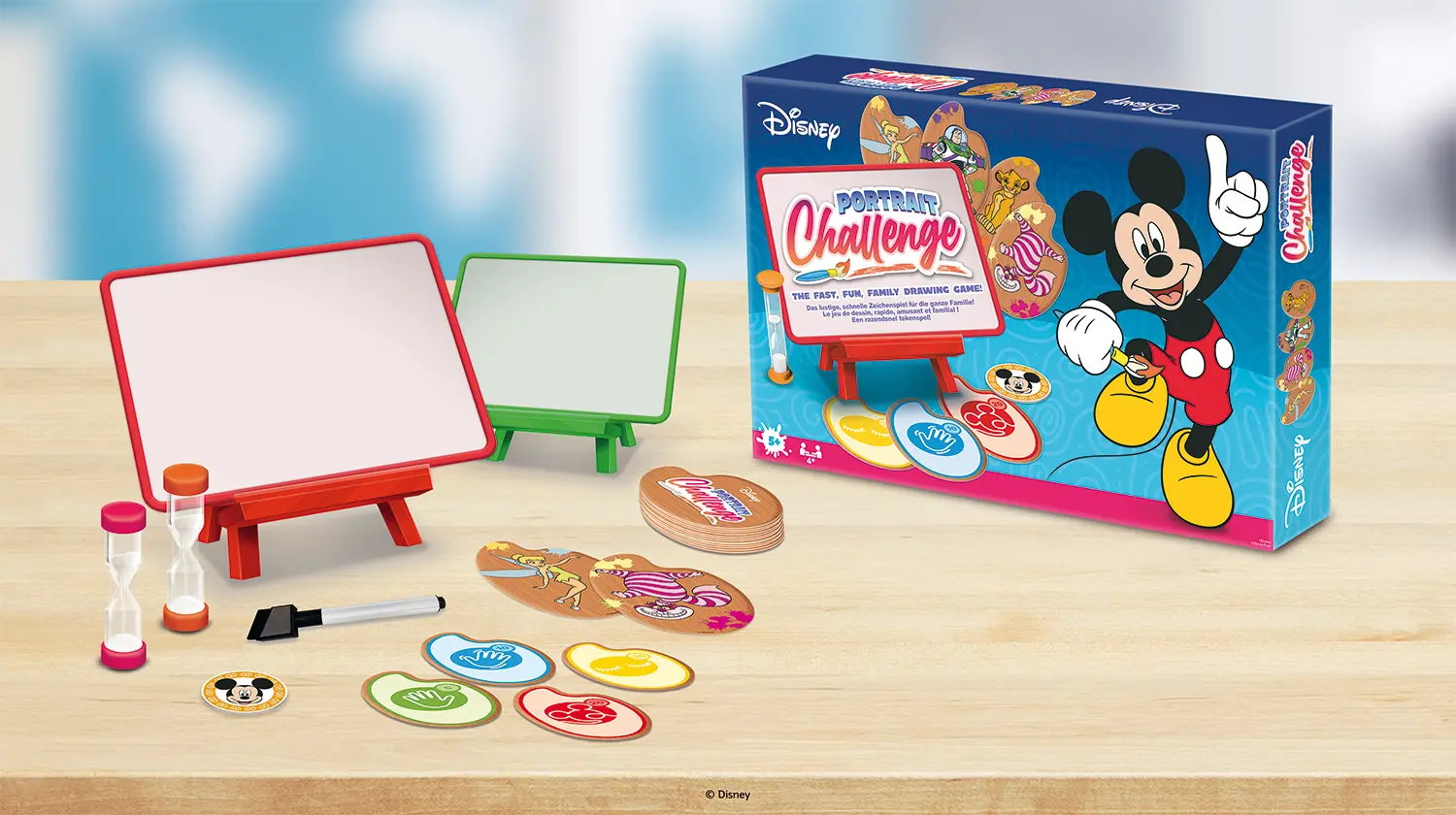 Die Spielinhalte des Disney Portrait Challenge liegen auf einem Holztisch als Hintergrund, die Schachtel steht daneben.