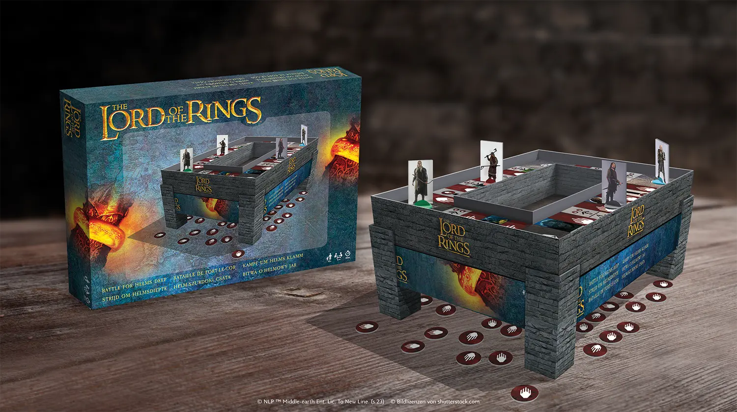 Es sind die Spielkomponenten des Lord of the Rings Helms Deep Spiels auf einem Holztisch zu sehen, im Hintergrund steht die Schachtel.