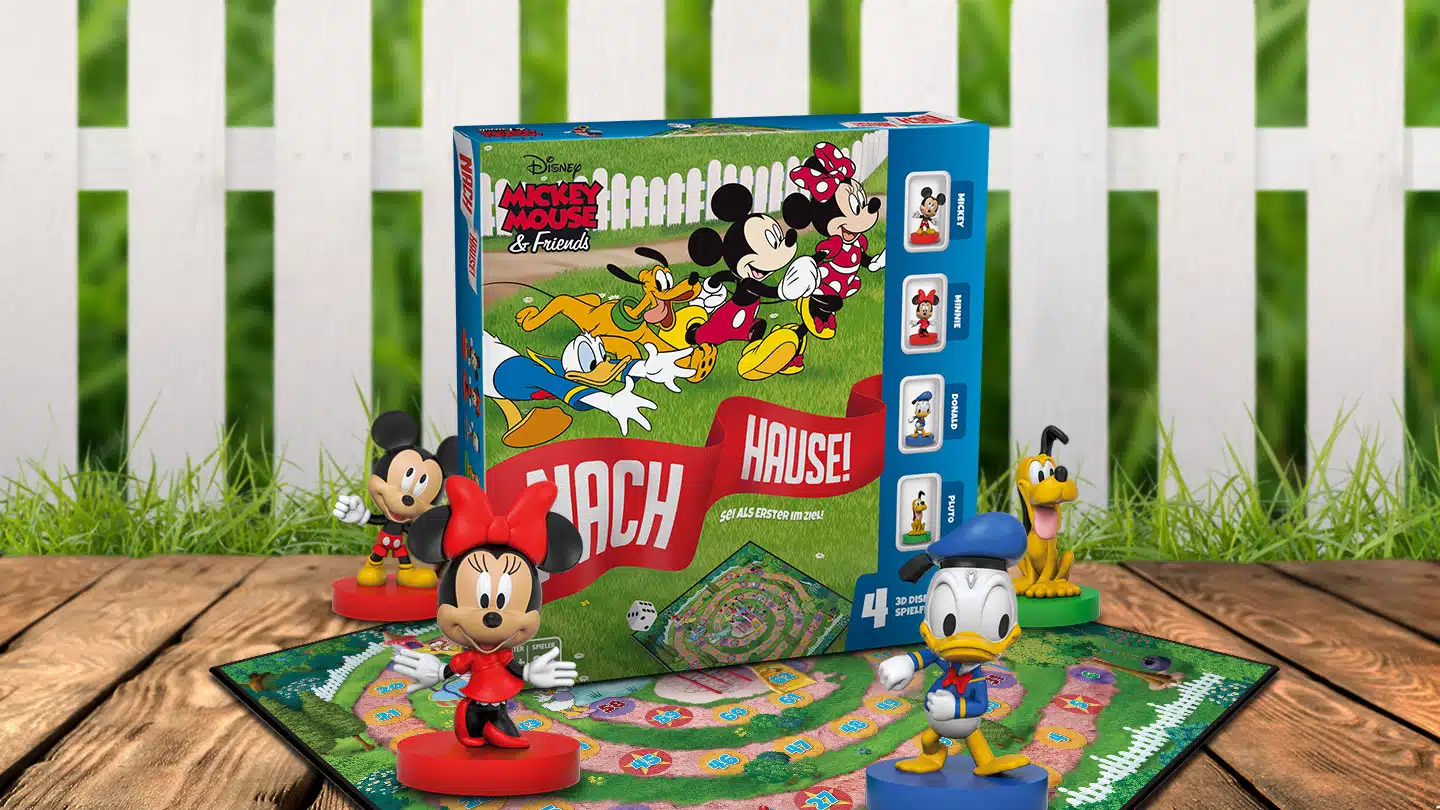 Das Mickey Mouse Nach Hause Spiel steht auf einem Untergrund aus Holz vor einem weißem Gartenzaun. Das Spielbrett liegt unter der Spielverpackung und es stehen die Figuren von Mickey, Minnie, Donald und Pluto um das Spiel herum.