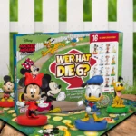 Das Mickey Mouse Wer hat die Sechs Spiel steht auf einem Untergrund aus Holz vor einem weißem Gartenzaun. Das Spielbrett liegt unter der Spielverpackung und es stehen die Figuren von Mickey, Minnie, Donald und Pluto um das Spiel herum.