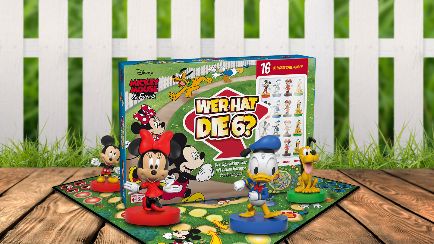 Das Mickey Mouse Wer hat die Sechs Spiel steht auf einem Untergrund aus Holz vor einem weißem Gartenzaun. Das Spielbrett liegt unter der Spielverpackung und es stehen die Figuren von Mickey, Minnie, Donald und Pluto um das Spiel herum.