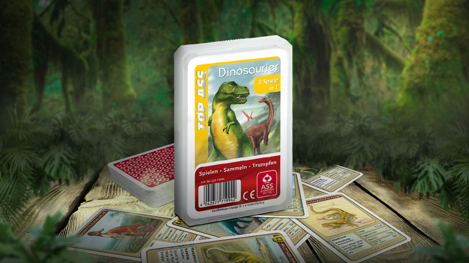 Das Top ASS Dinosaurier Trumpfspiel steht in einem Urwald auf einem hölzernen Untergrund. Unter dem Spiel liegen einige der dazugehörigen Spielkarten.