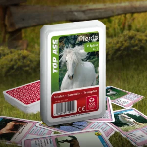 Das Top ASS Pferde Trumpfspiel steht auf einer Wiese, unter dem Spiel liegen einige der dazugehörigen Spielkarten. Im Hintergrund steht ein Zaun der eine anschließende Weide abgrenzt.
