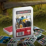 Das Top ASS Traktoren Trumpfspiel steht auf einer Wiese, unter dem Spiel liegen einige der dazugehörigen Spielkarten. Im Hintergrund steht ein Zaun der eine anschließende Weide abgrenzt.