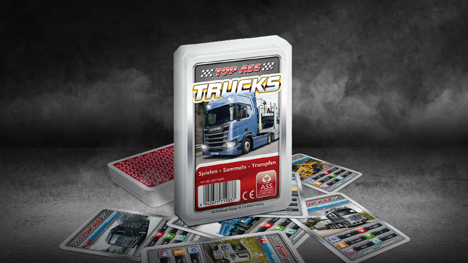 Das Top ASS Trucks Trumpfspiel steht auf einem Untergrund aus Asphalt, unter dem Spiel liegen die dazugehörigen Spielkarten. Der Hintergrund ist dunkel und es ist Rauch zu sehen.