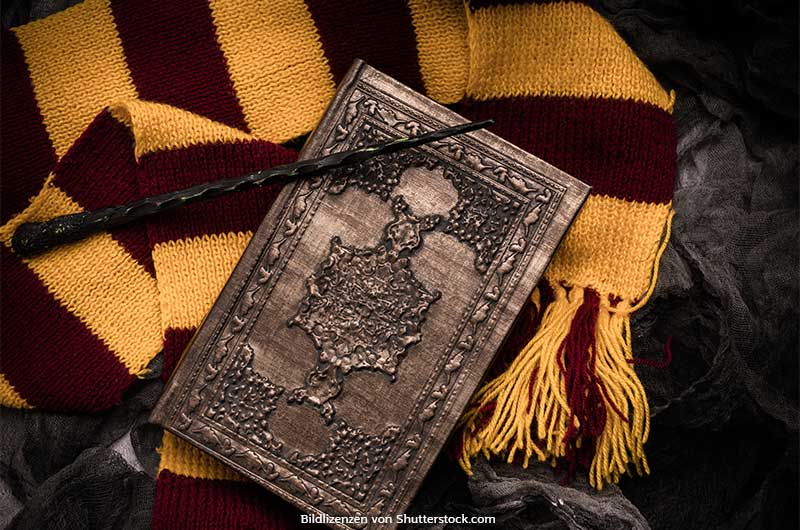 Altes Buch liegt auf rot-gelbem Schal neben Zauberstab. Harry Potter Spiele, ASS Altenburger