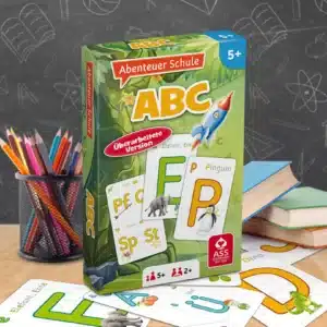 Das Abenteuer Schule ABC Spiel steht auf einem Schultisch. Unter dem Tisch liegen einige der dazugehörigen Spielkarten. Neben dem Spiel stehen Stifte und ein Bücherstapel. Im Hintergrund ist unscharf eine Tafel zu erkennen.