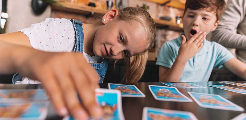 Ein Mädchen deckt eine Karte beim Memory auf, neben ihr sitzt ein erstaunter Junge. Lernspiele, ASS Altenburger