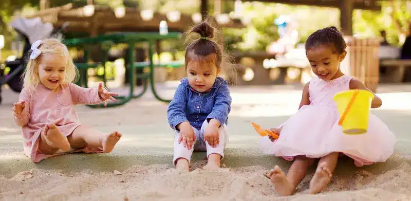 Drei Mädchen sitzen nebeneinander am Rand vom Sandkasten und spielen Kinderrechte ASS Altenburger