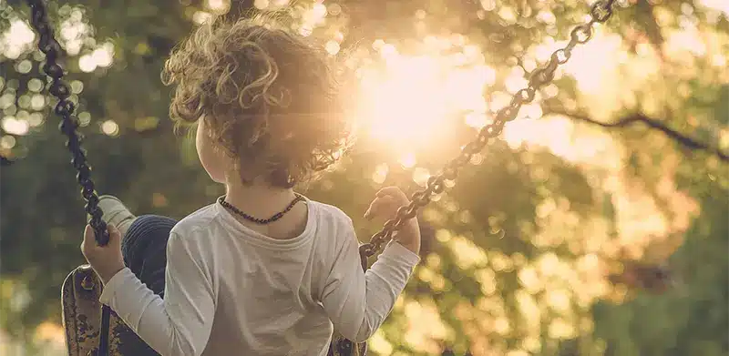 Junge schaukelt vor Bäumen durch die die Sonne scheint Kinderrechte ASS Altenburger