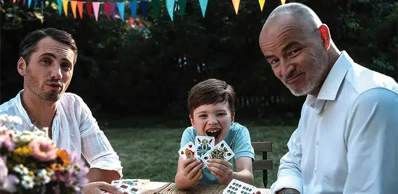 Opa, Vater und Sohn spielen gemeinsam Skat in einem Garten. Geschichte der Spielkarten, ASS Altenburger