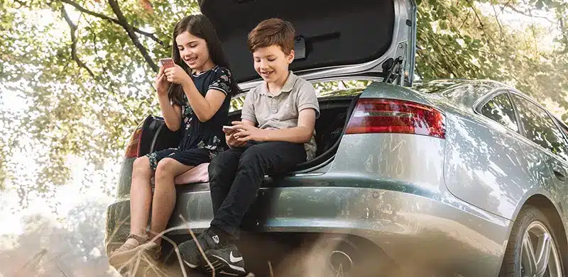 Zwei Kinder sitzen auf Kofferraum-Klappe und spielen Kartenspiel TOP ASS. Kindertag, ASS Altenburger