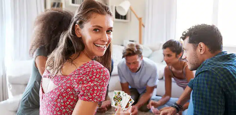 Freunde spielen Karten, eine Frau dreht sich zur Kamera und zeigt ihr Kartenblatt. Kartenkultur, ASS Altenburger