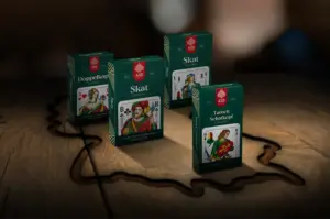 Kartenspiele Doppelkopf, Skat und Tarock stehen auf dem Tisch umrandet vom Umriss Deutschlands. Kartenkultur, ASS Altenburger
