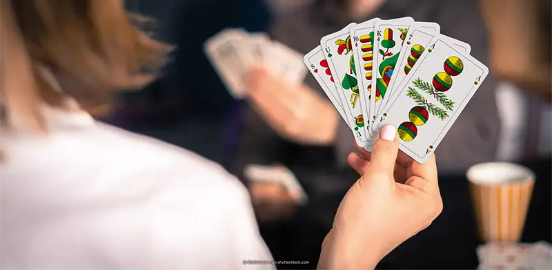 Frau hält Spielkarten von Kartenspiel Schafkopf mit Fränkischem Bild. ASS Altenburger
