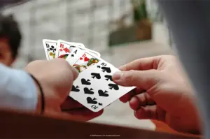 Nahaufnahme von zwei Händen, die Spielkarten mit Symbolen Herz, Pik, Karo und Kreuz halten. Kartenfarben, ASS Altenburger